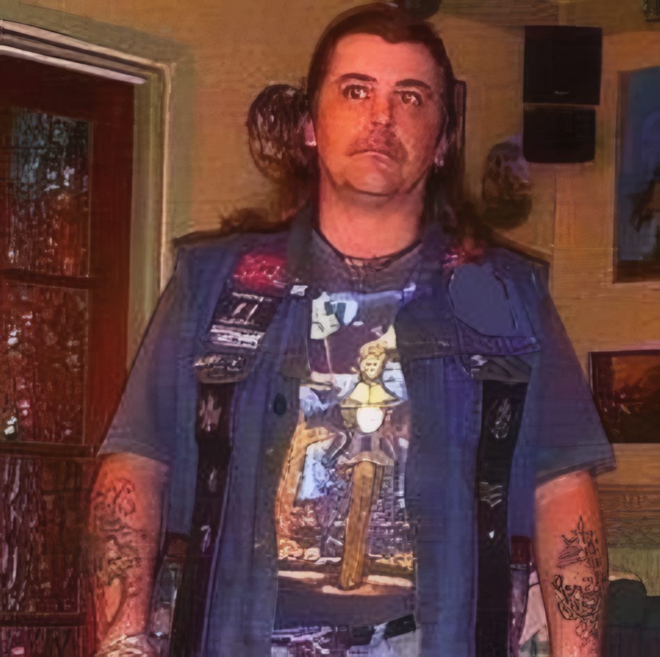 John in a denim cut-off waistcoat over a T-shirt, tattoos down both forearms.