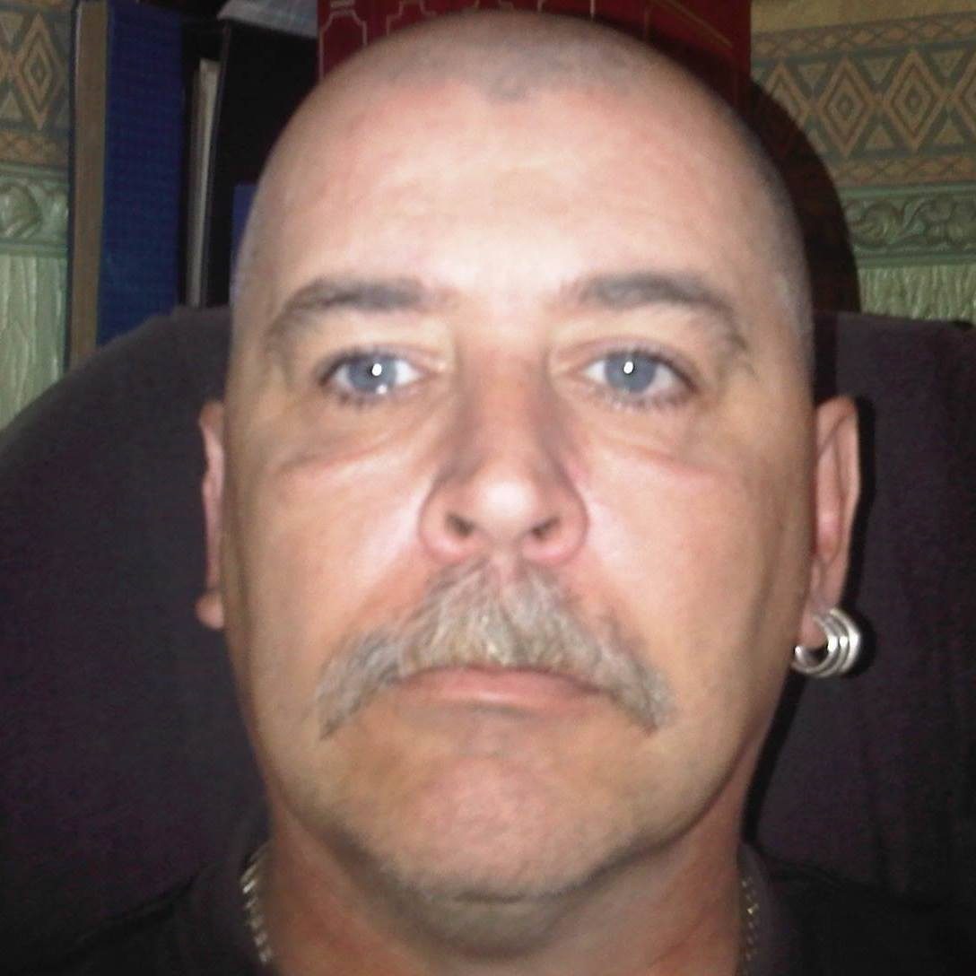 John, close up, looking straight at the camera. Close-cropped hair, a grey moustache and a hoop earring.